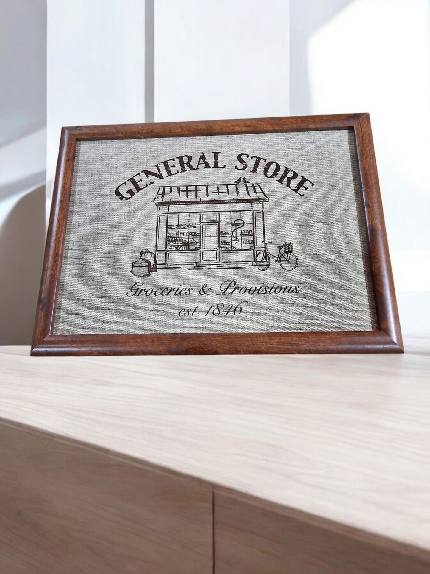 Framed print lap tray of a vintage general store design, featuring a building illustration, "Groceries & Provisions," and "est. 1846".