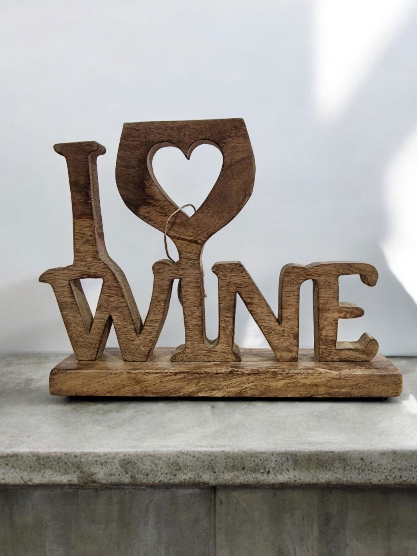 Wooden decorative sign that says "I love wine" with a heart-shaped cut-out in a wine glass design, situated on a woven placemat.
