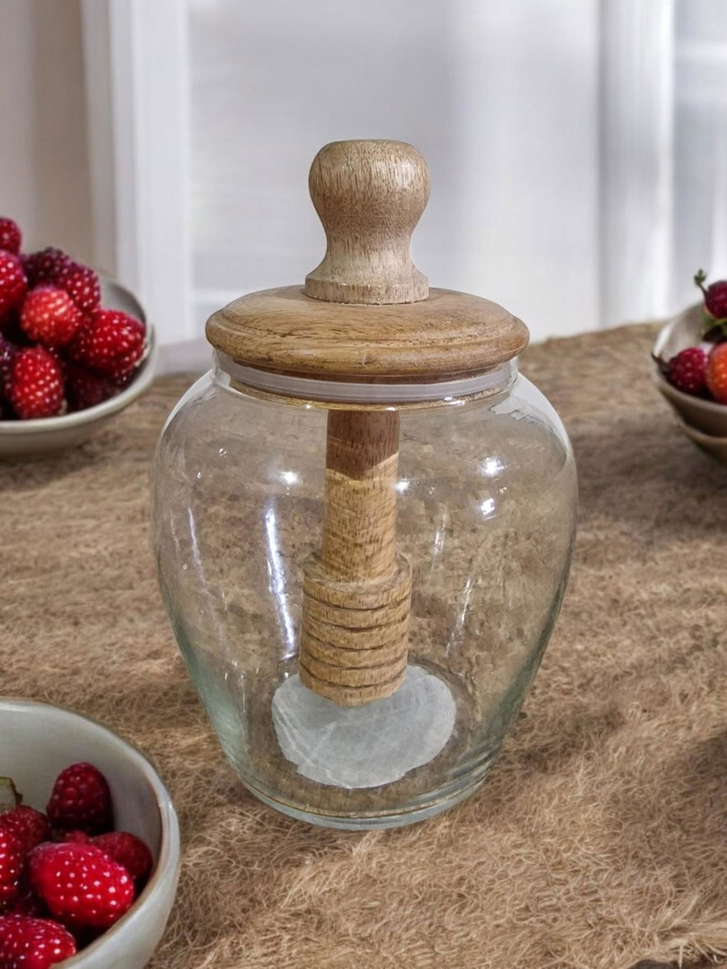 Clear glass jar with a wooden lid and dipper, sitting on a burlap table.