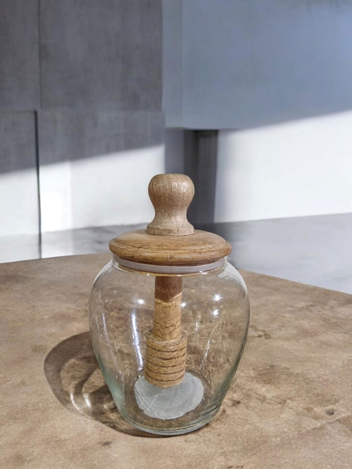 Clear glass jar with a wooden lid and dipper, sitting on a burlap table.