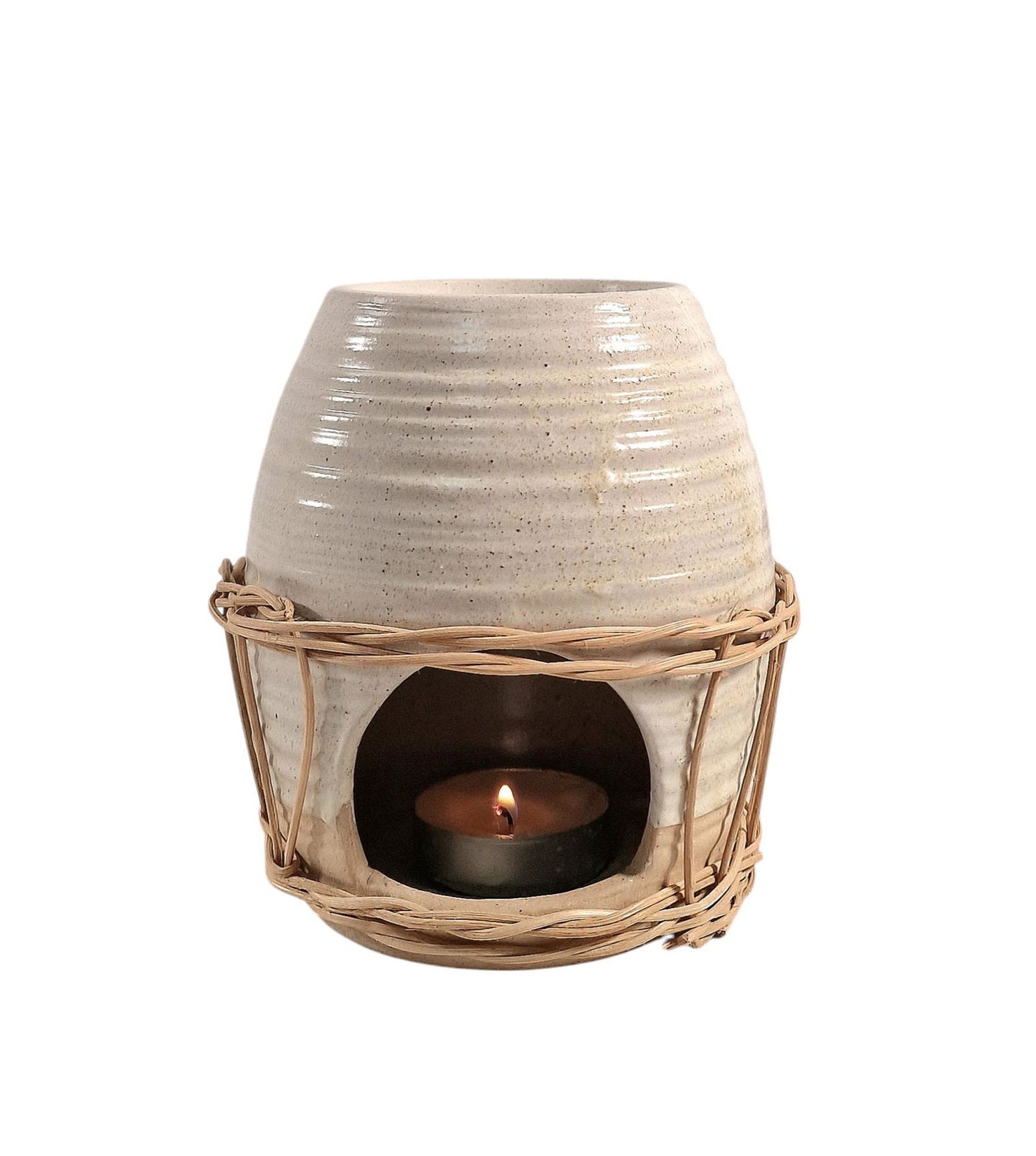 Ceramic oil burner with natural rattan detail, featuring a lit tealight inside, styled on a wooden surface with a floral arrangement in the background